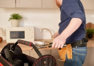 young plumber wearing work outfit and black bag of plumbing tools repairing a kitchen sink